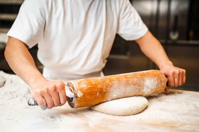 Ein Bäcker rollt auf einer bemehlten Arbeitsfläche den Brotteig aus.