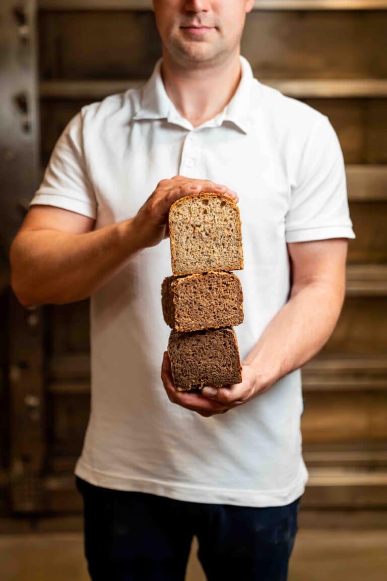 Ein Bäcker hält drei frisch gebackene Brote in seiner Hand.