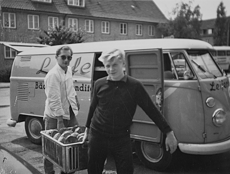 Ein historisches schwarz-weiß Bild zeigt den Gründer Herrn Leifert und einen Mitarbeiter beim Ausladen von Broten aus einem Lieferwagen.