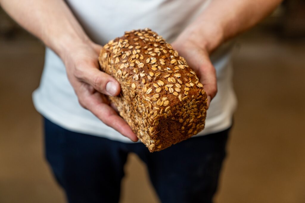 Ein Bäcker hält ein frisch gebackenes Vollkornbrot.