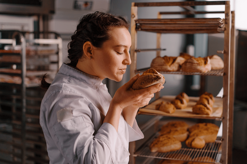 Eine Bäckerin riecht genüsslich an frisch gebackenem Brot.