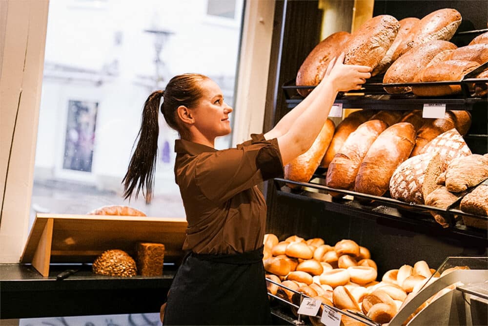 Eine Verkäuferin von Leifert nimmt einen Leib Brot aus dem Regal.