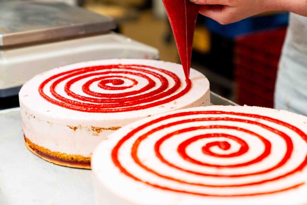 Ein Mitarbeiter trägt Erdbeercreme auf einen Kuchen auf.